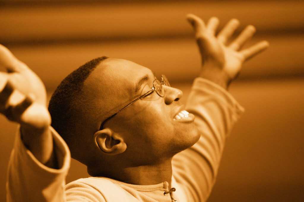 A man wearing eye glasses raising his hands in joy